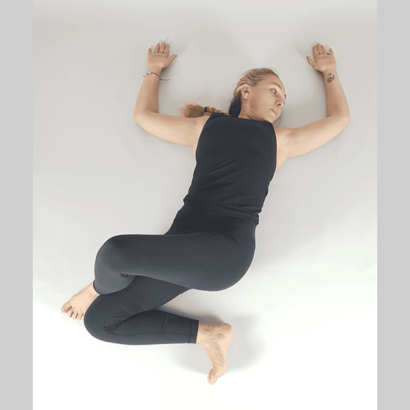 Yoga practitioner resting in Supine Twist with arms wide open.