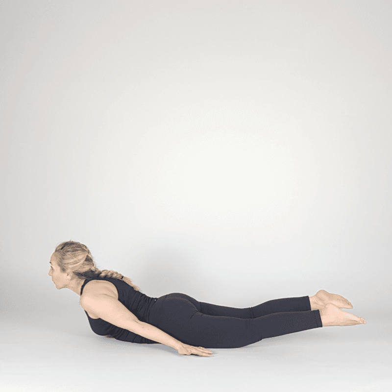 Yoga practitioner in Locust Pose with arms reaching back.