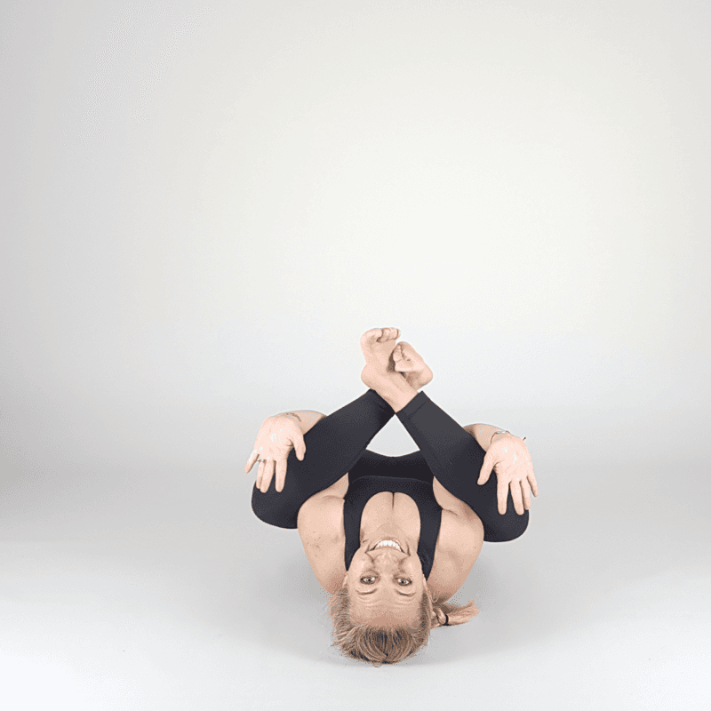 Yoga practitioner in supine hip release with crossed ankles.
