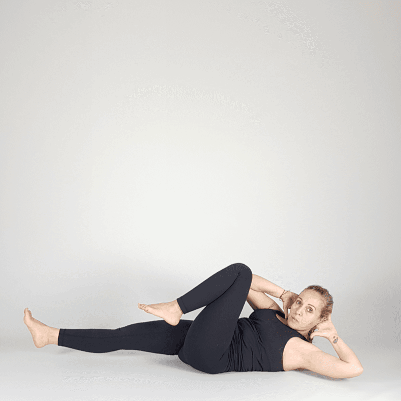 Yoga practitioner hugging knee to chest on the mat.