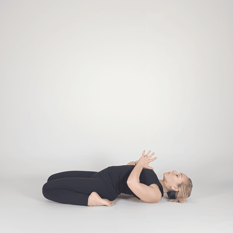 Yoga practitioner resting in Reclined Hero with hands on heart.