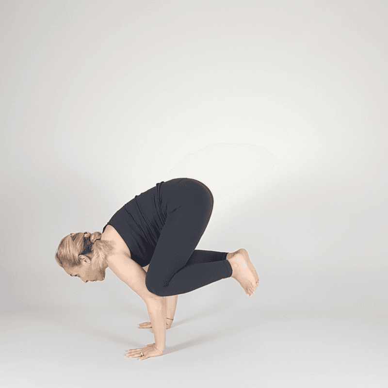 Yoga practitioner balancing in Crow Pose with knees on arms.