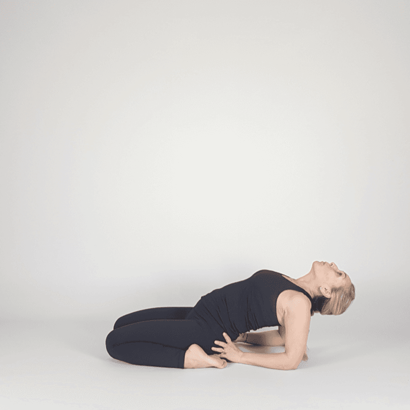 Yoga practitioner reclining in Hero Pose with gentle backbend.