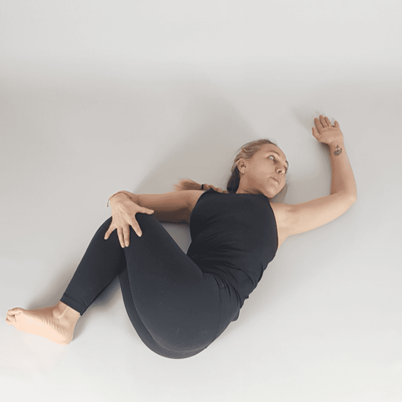 Yoga practitioner in reclined spinal twist with knees to side.