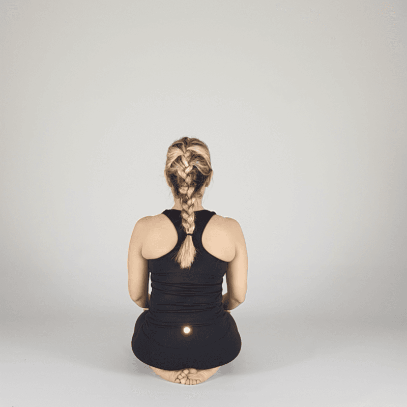 Yoga practitioner seated in Hero Pose viewed from behind.
