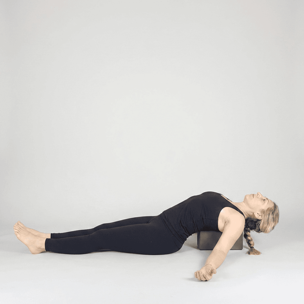 Woman in Supported Fish Pose reclining over a yoga block placed under the upper back