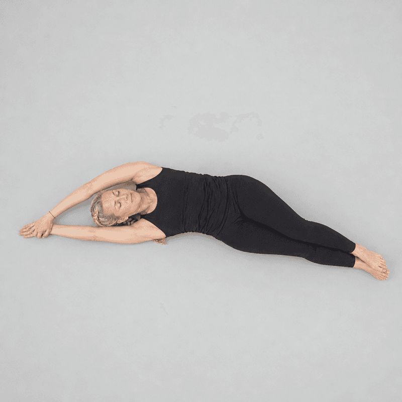 Overhead view of a woman lying on her back curved into a crescent side bend, arms overhead holding one wrist