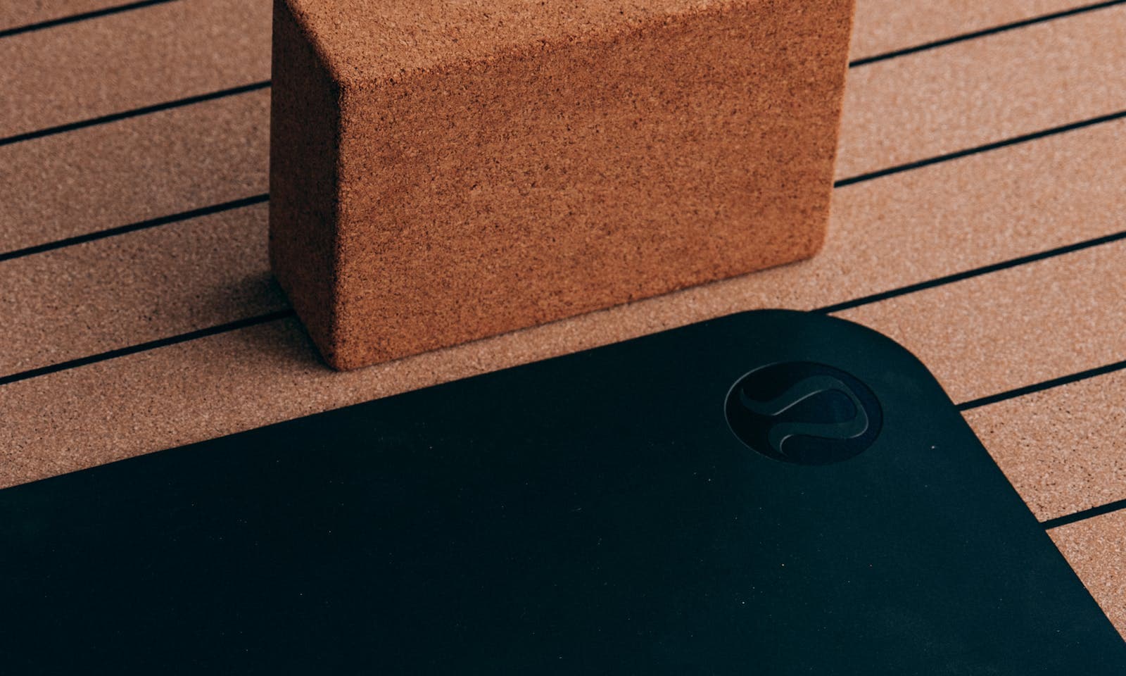 Cork yoga block on a striped yoga mat — the prop choice that shows up in every class