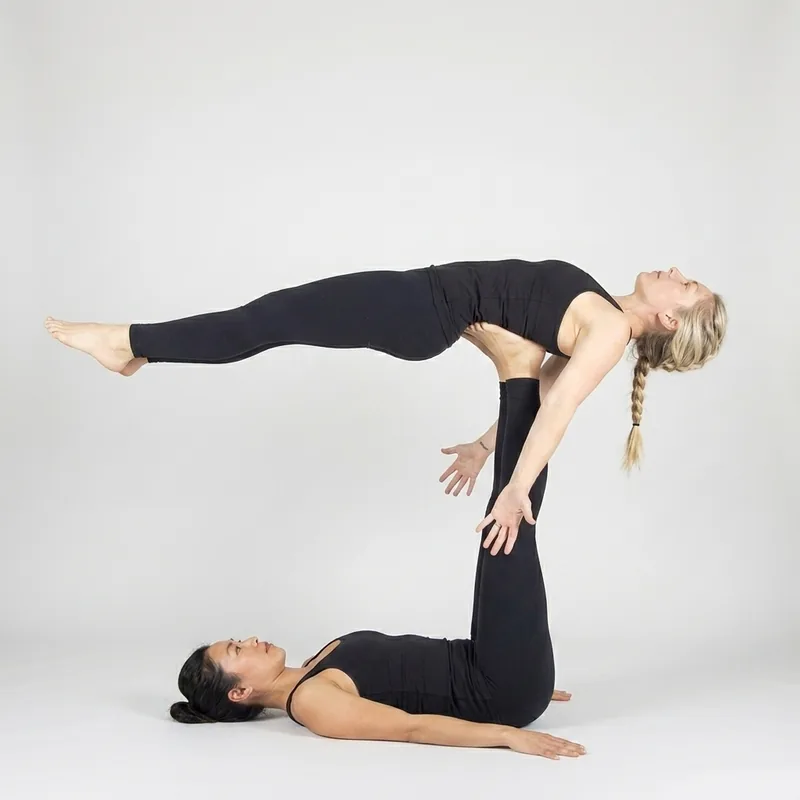 Acro yoga pose for 2 people — Whale, the base lying on her back supporting the flyer face up on the soles of her feet